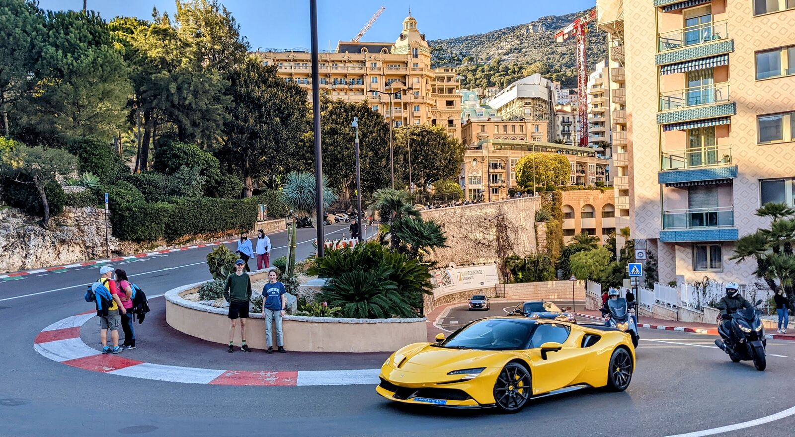 A yellow sports car at a Monaco roundabout, watched by a small group of onlookers